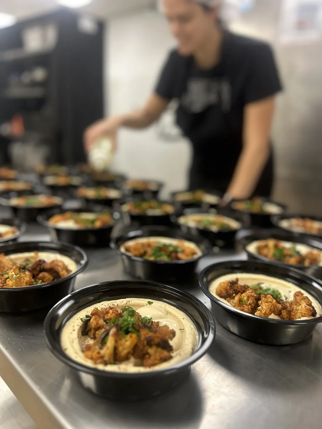 Rows of roasted cauliflower hummus bowls being finished in the kitchen